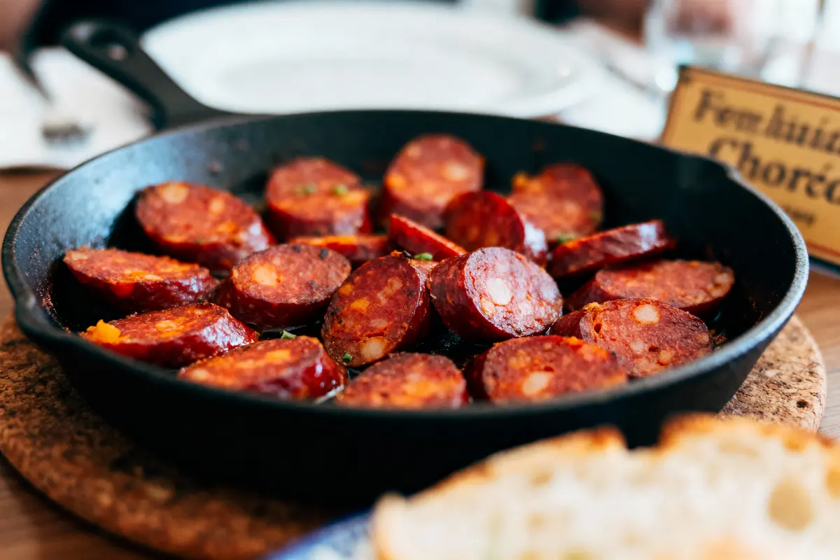 Tranches de chorizo dans une poêle en fonte, pain à l'avant-plan, table de restaurant.