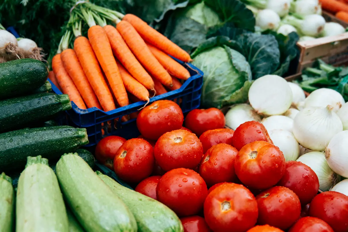 Carottes, tomates, courgettes et oignons frais exposés sur un étal de marché, entourés de feuilles de chou.