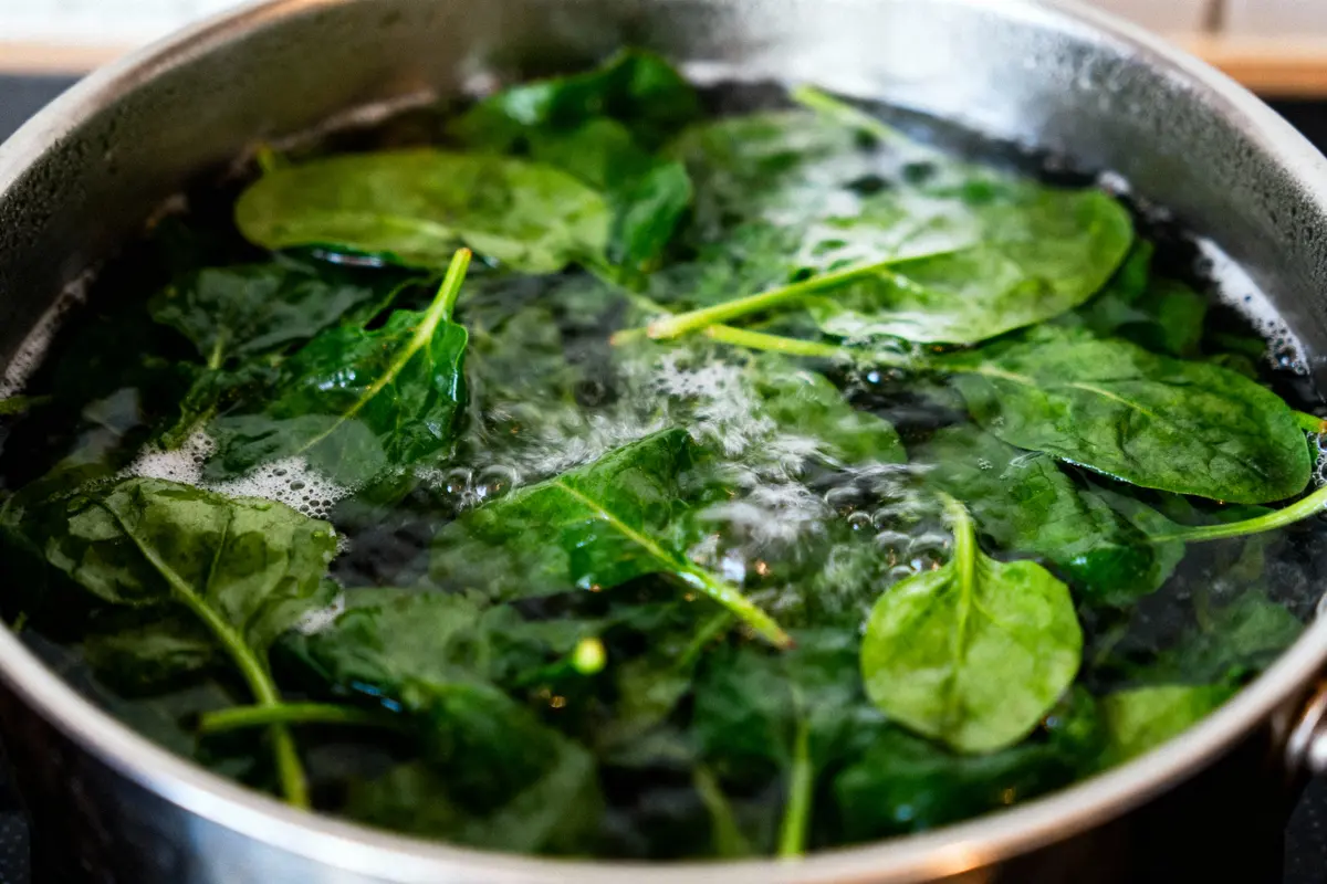Feuilles d'épinards bouillant dans une casserole d'eau sur une cuisinière.