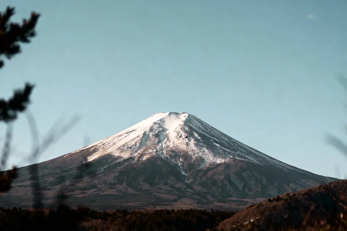 Montagne enneigée sous ciel bleu clair, entourée de végétation sombre au premier plan.
