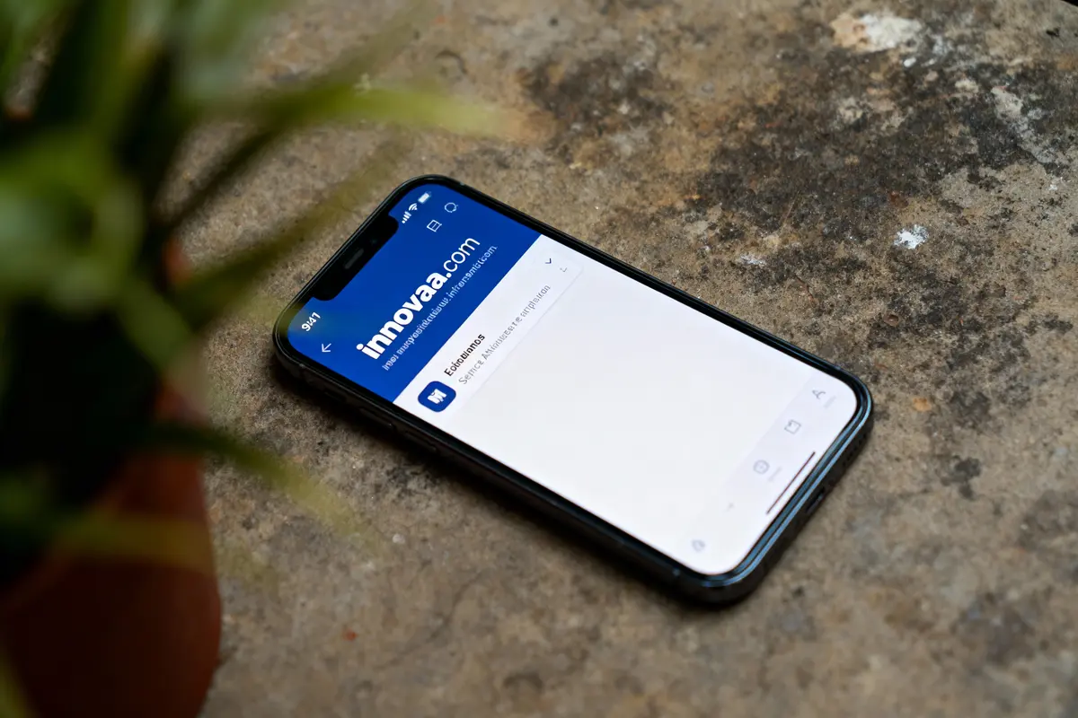 Smartphone sur surface rugueuse affichant site "innova.com". Plante floue au premier plan, coin gauche.