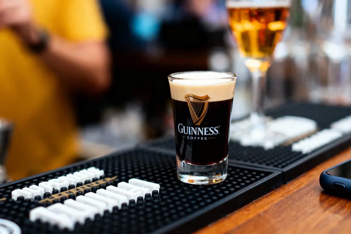 Verre de Guinness sur un bar, avec une boisson dorée en arrière-plan.