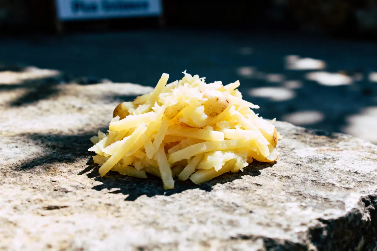 Tas de pommes de terre râpées, posé sur une surface en pierre, éclairé par le soleil.