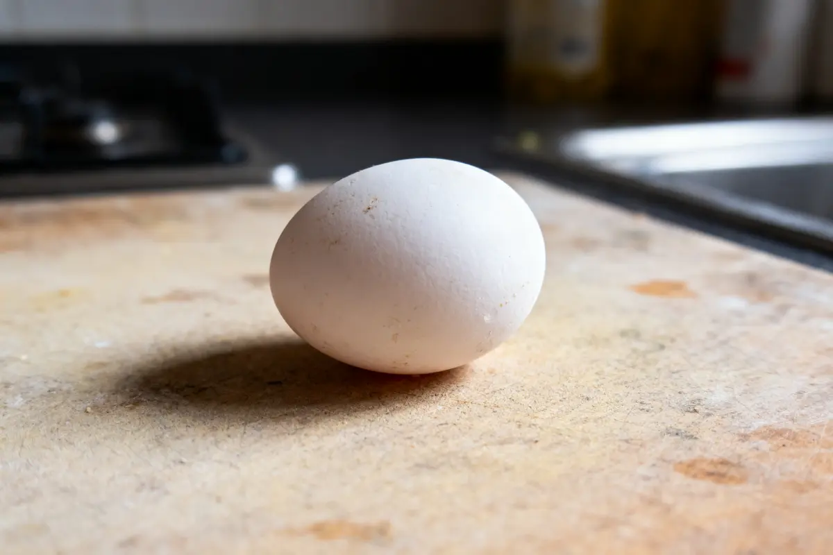 Un oeuf blanc posé sur une planche de bois dans une cuisine.
