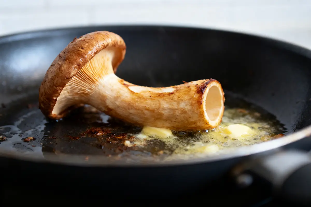 Champignon rôti entier dans une poêle noire avec beurre fondu, sur fond de cuisine.