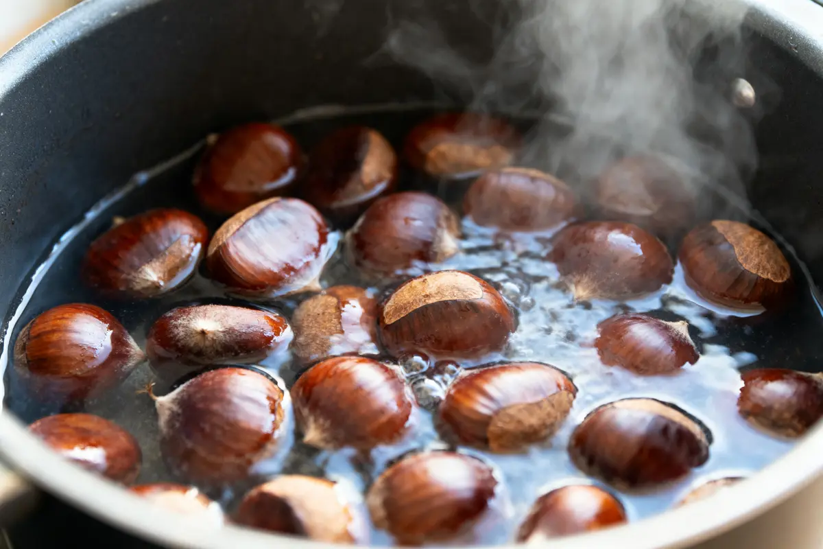 Châtaignes brunes bouillantes dans une casserole, vapeur visible, eau frémissante.