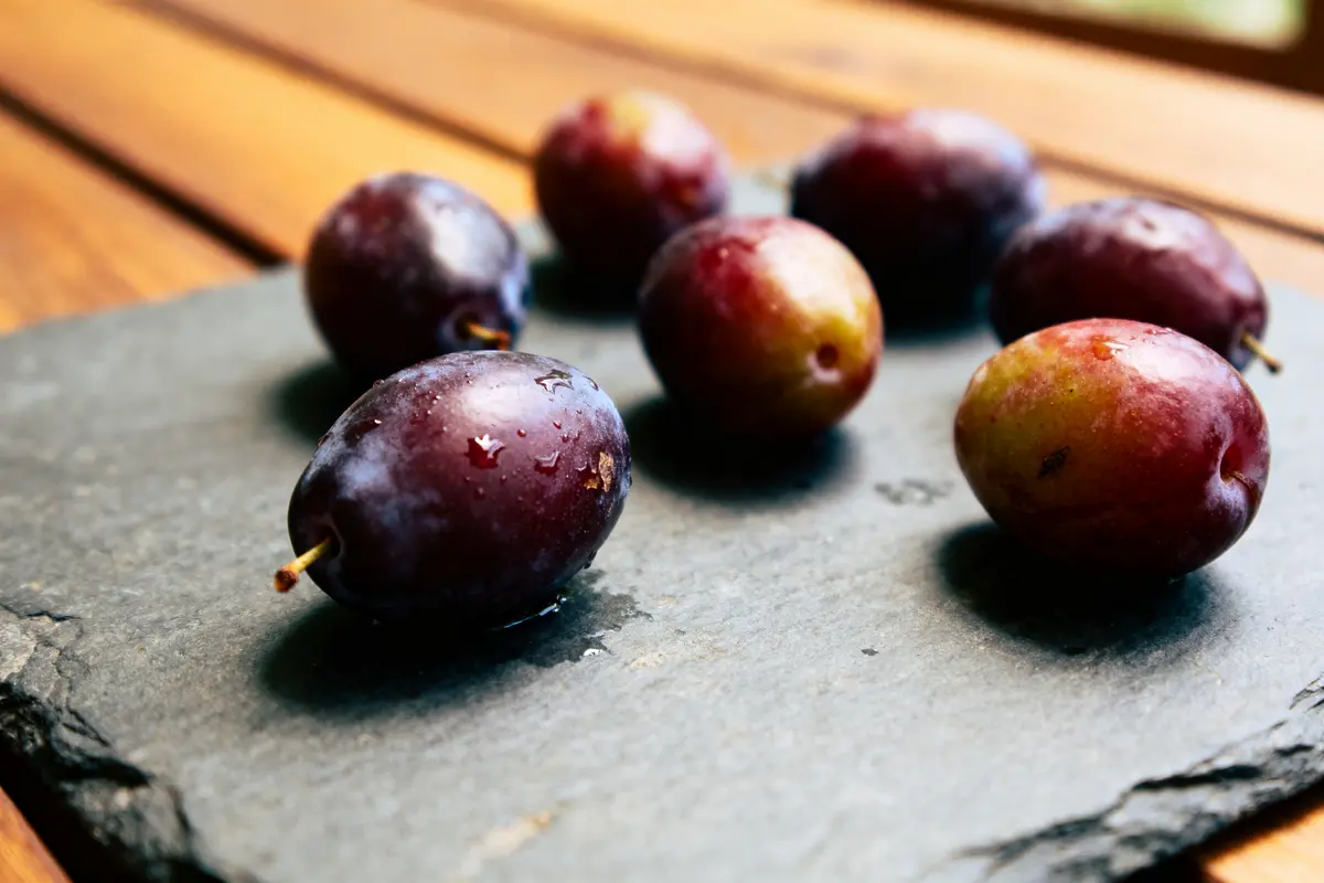 Prunes violettes brillantes sur ardoise noire, table en bois en arrière-plan.