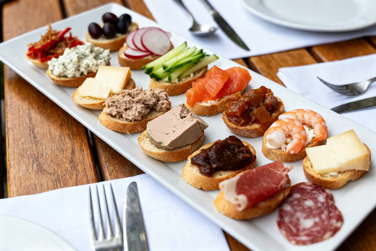 Assortiment de canapés variés sur une assiette blanche, posée sur une table en bois avec couverts.