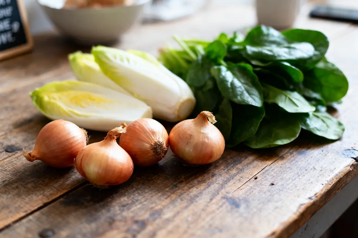 Oignons, endives et épinards frais sur table en bois rustique.