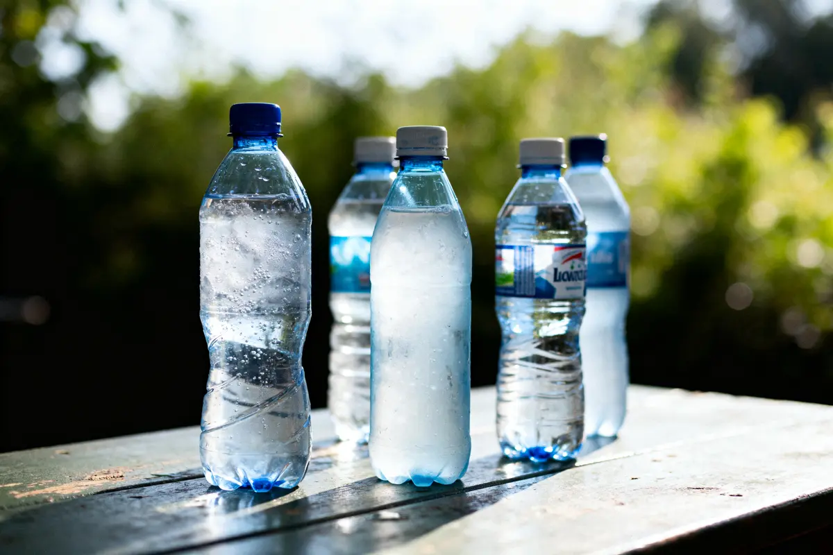 Cinq bouteilles d'eau en plastique sur une table extérieure, éclairées par le soleil, avec arrière-plan flou.