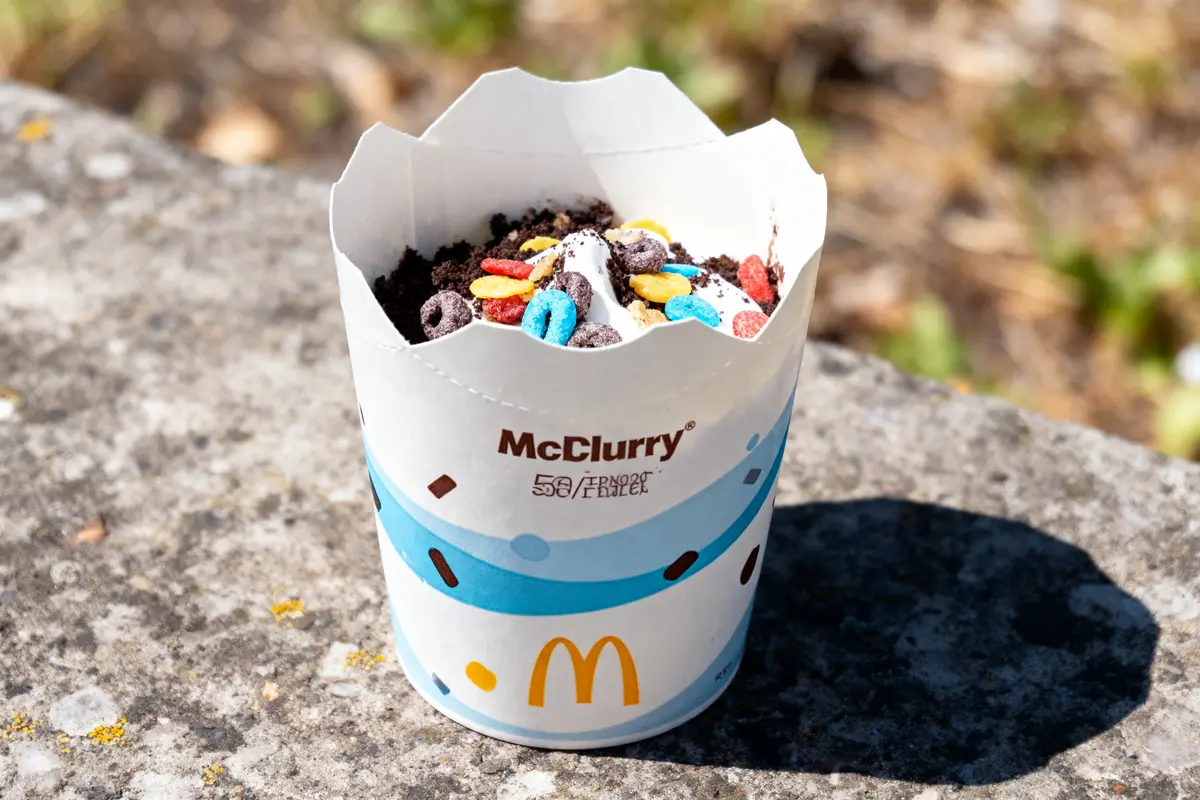 Un pot de McFlurry avec des céréales colorées et morceaux de chocolat, posé sur une surface en pierre.