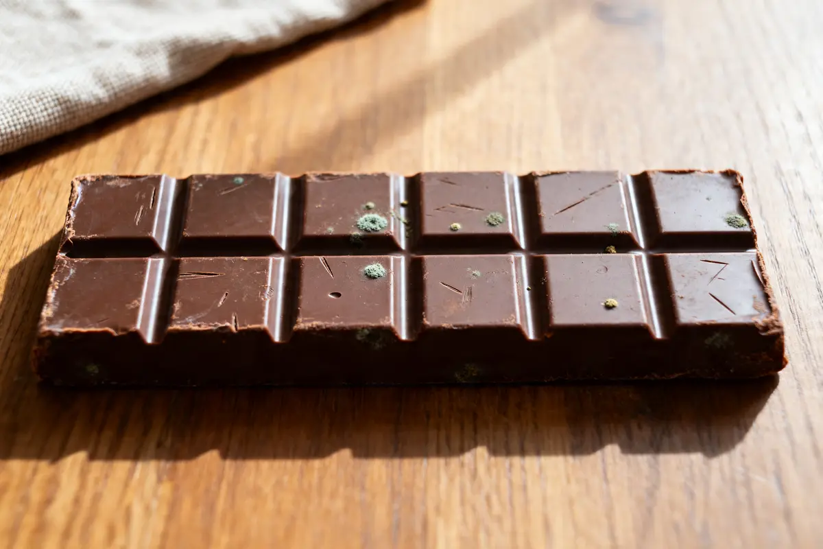 Tablette de chocolat périmé avec moisissures visibles sur une table en bois.