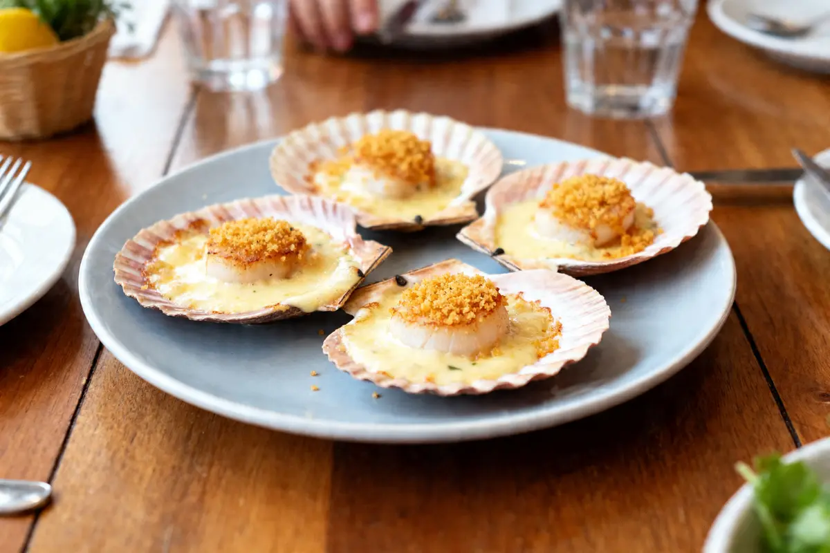 Quatre coquilles Saint-Jacques à la bretonne gratinées servies sur une assiette bleue