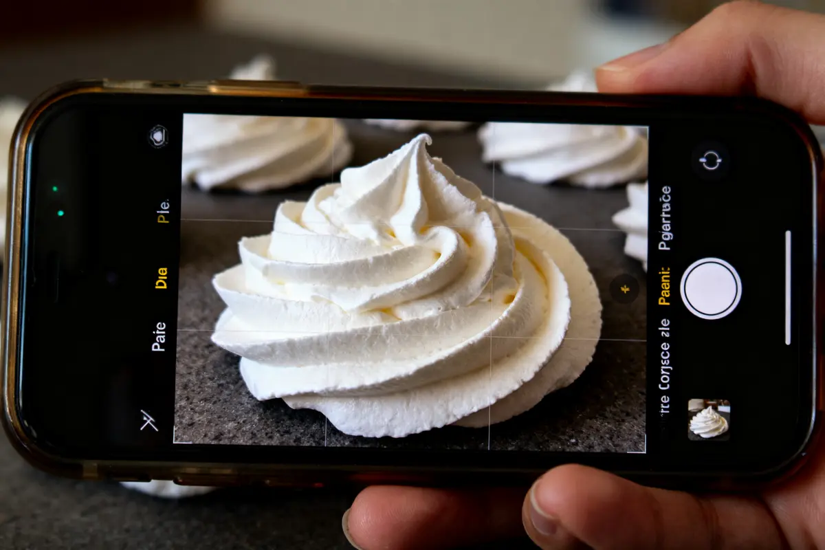 Photo de meringue blanche sur smartphone, posée sur table en arrière-plan flou.